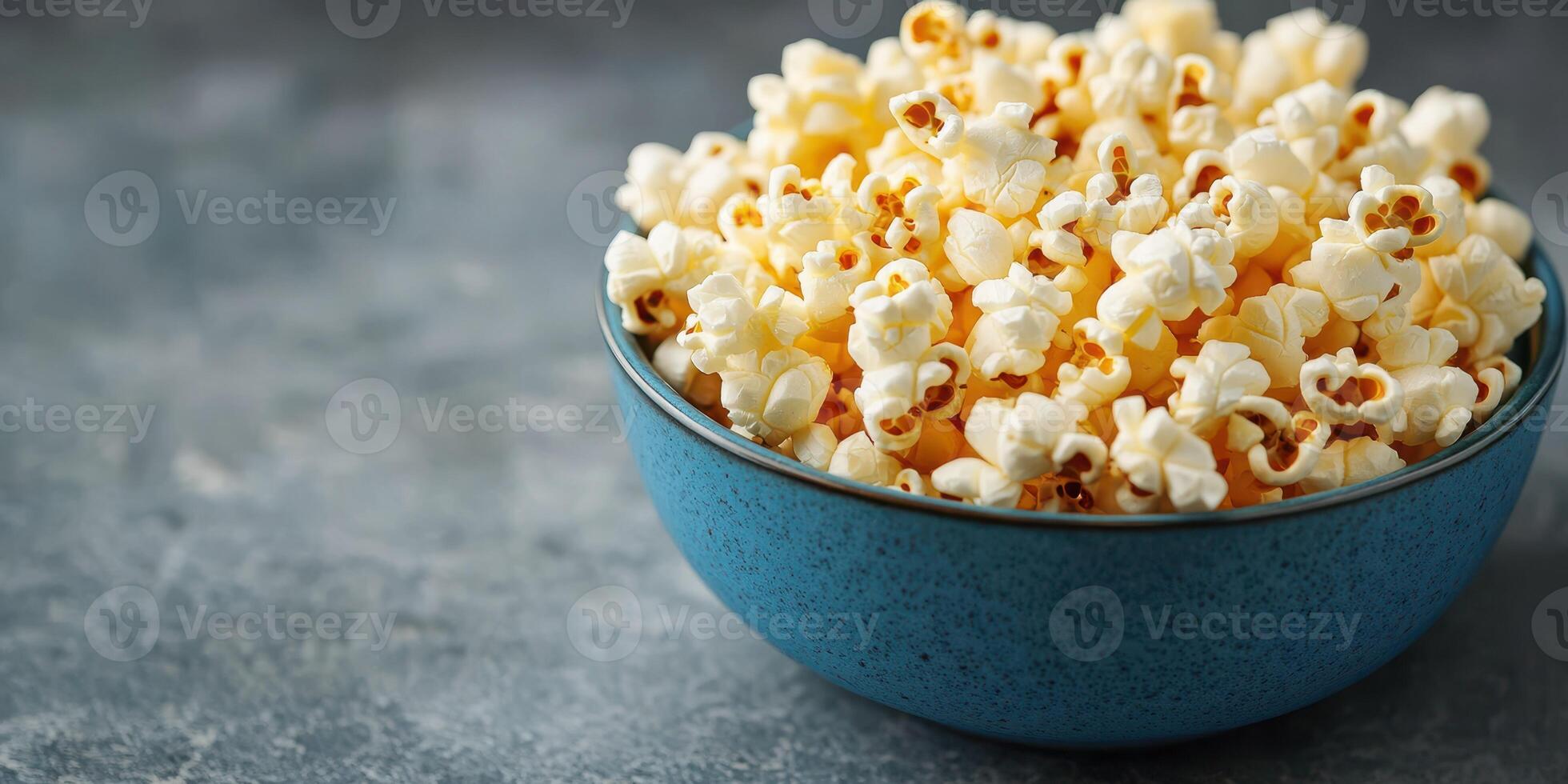 Bowl of freshly popped popcorn on a textured gray surface ready for snacking during movie night photo