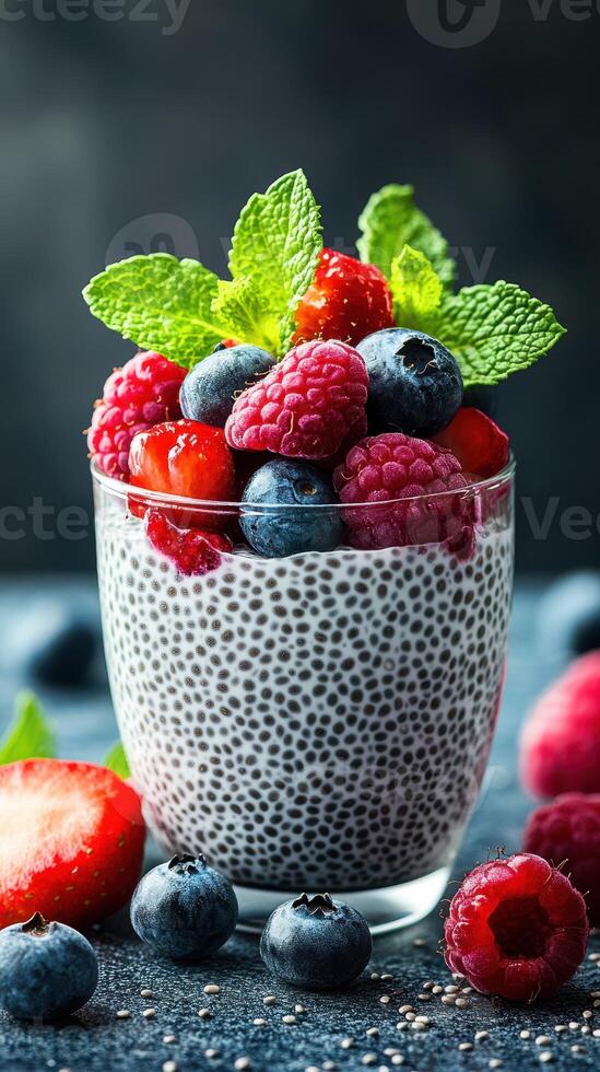 Chia seed pudding topped with fresh berries and mint leaves served in a clear glass against a dark background photo