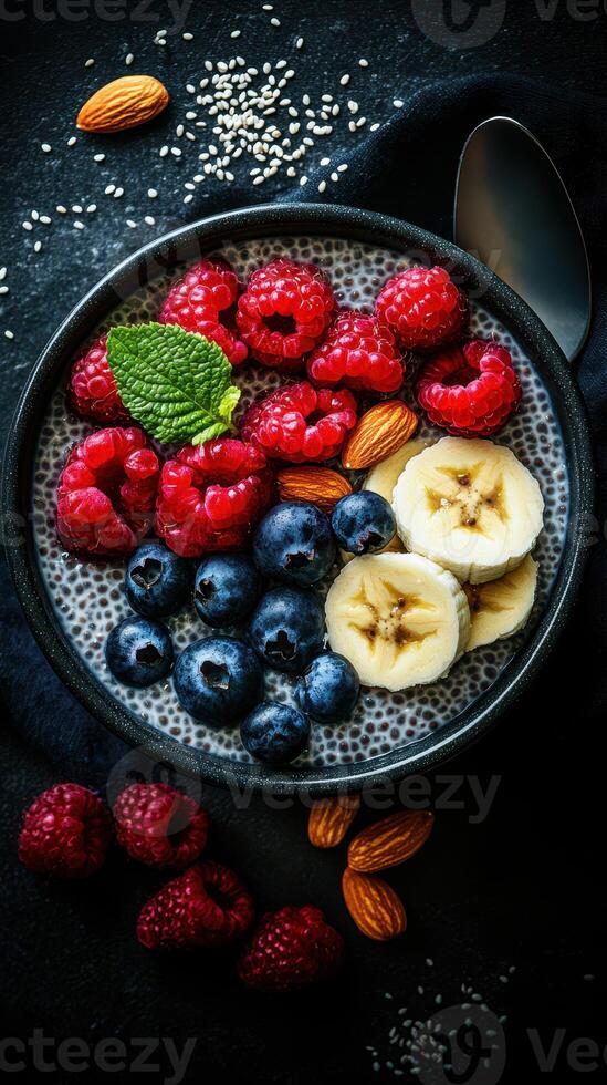 Chia seed pudding topped with fresh berries and banana slices served in a dark bowl photo