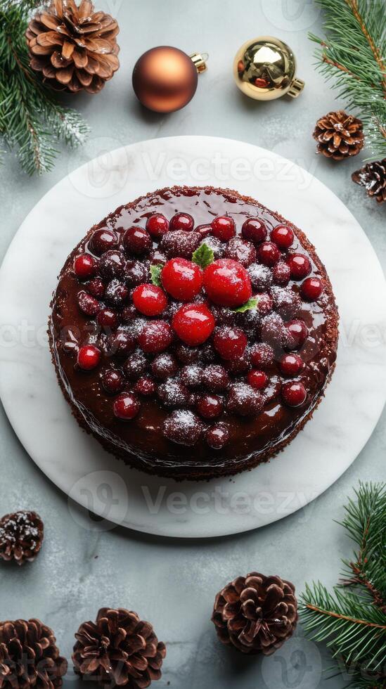 Stunning chocolate cake decorated with red berries and mint on a marble platter surrounded by festive pinecones photo