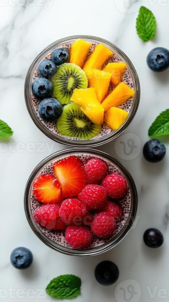 Colorful fruit bowls with chia pudding displayed on a marble countertop surrounded by fresh blueberries and mint leaves photo