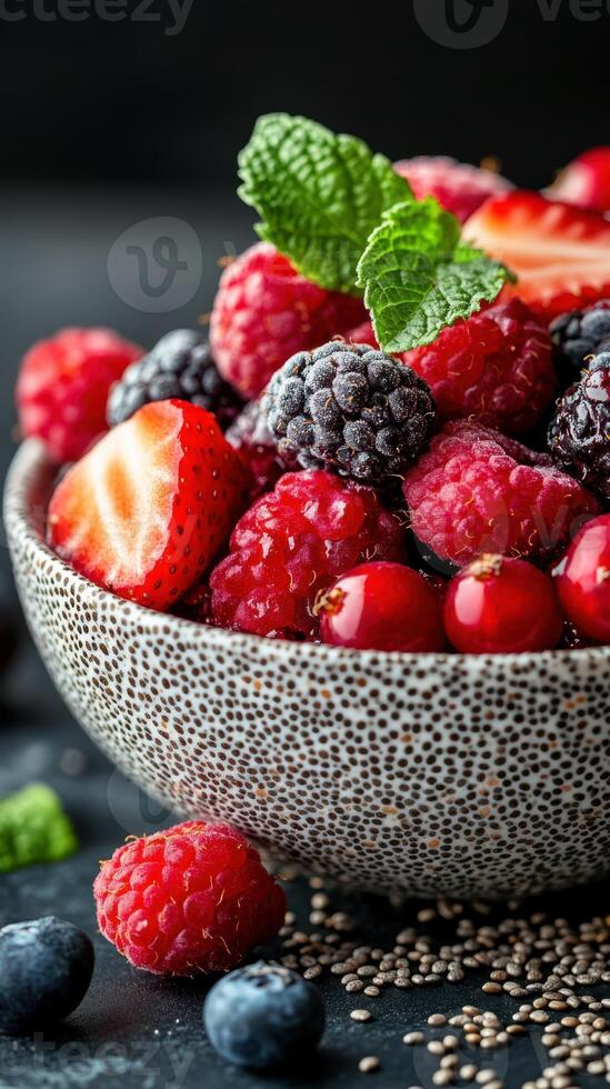 Fresh mixed berries in a decorative bowl with mint leaves on a dark background photo