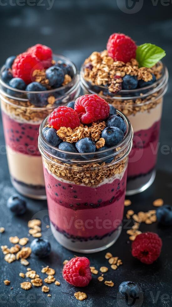 Colorful dessert jars filled with layers of yogurt, berries, and granola displayed on a dark background photo
