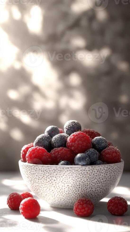 Fresh raspberries and blueberries in a textured bowl illuminated by soft natural light photo