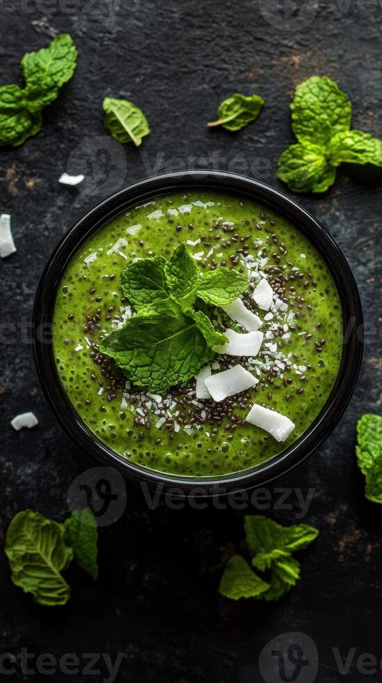 Smoothie bowl prepared with fresh ingredients and garnished with mint leaves and coconut flakes on a dark surface photo