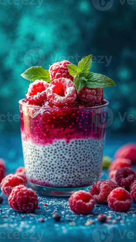 Raspberry chia pudding in a glass topped with fresh berries and mint leaves on a vibrant blue background photo