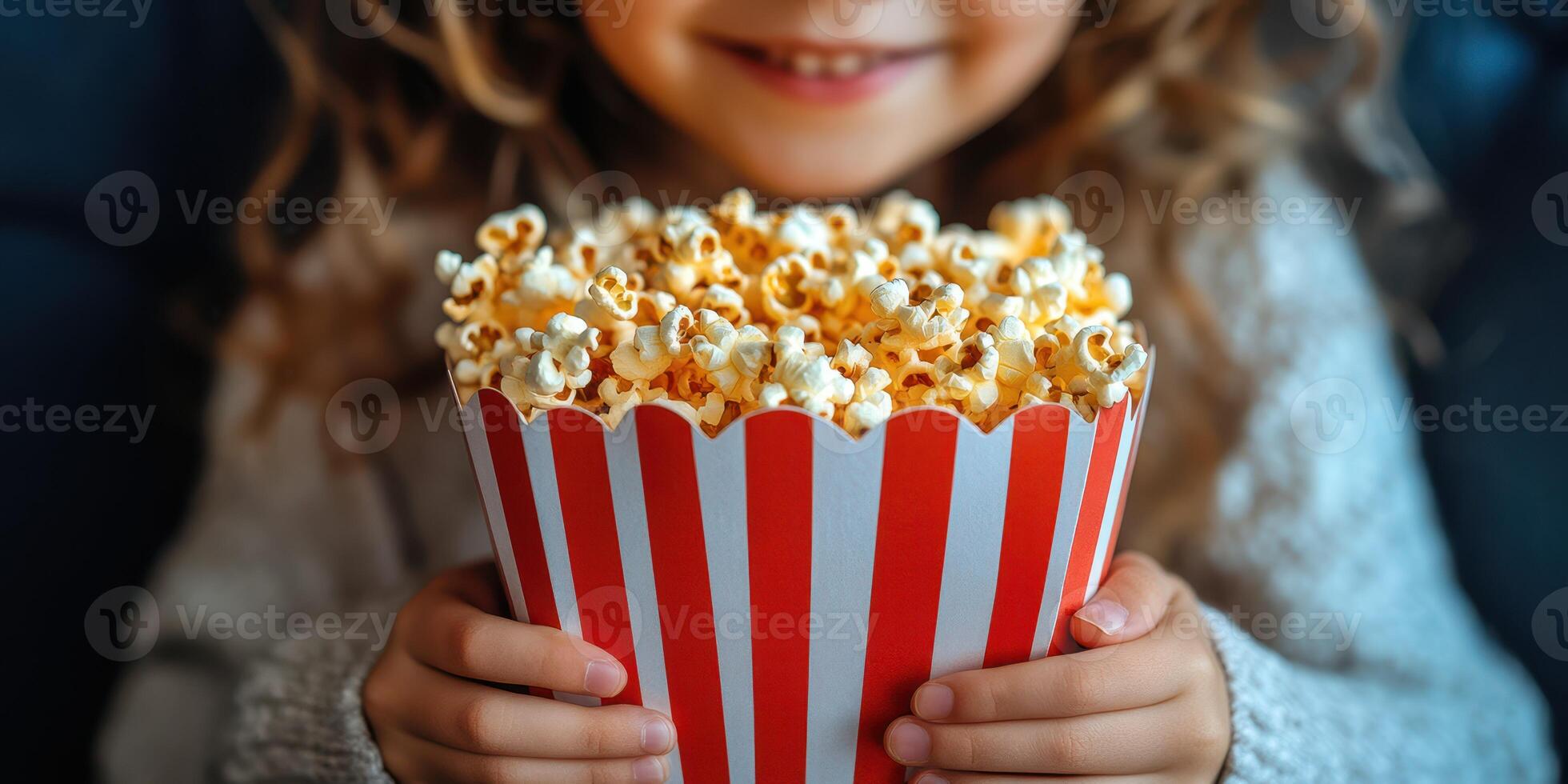 Young child enjoys a large bowl of popcorn while smiling warmly in a cozy indoor setting photo