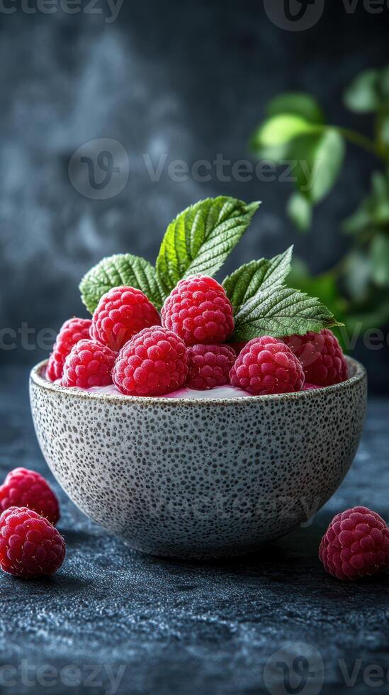 Fresh raspberries arranged in a textured bowl with mint leaves on a dark background, showcasing vibrant colors photo