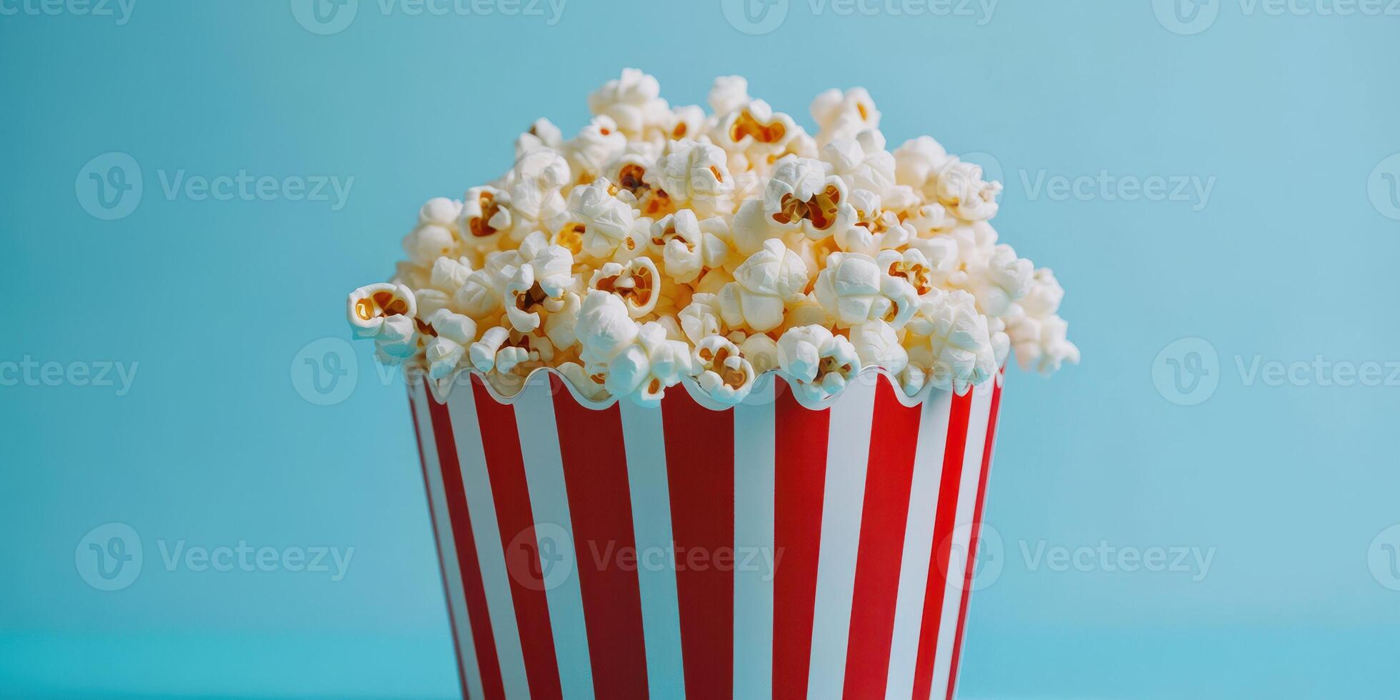 Enjoying a fresh bucket of buttery popcorn against a bright blue background while watching a movie photo