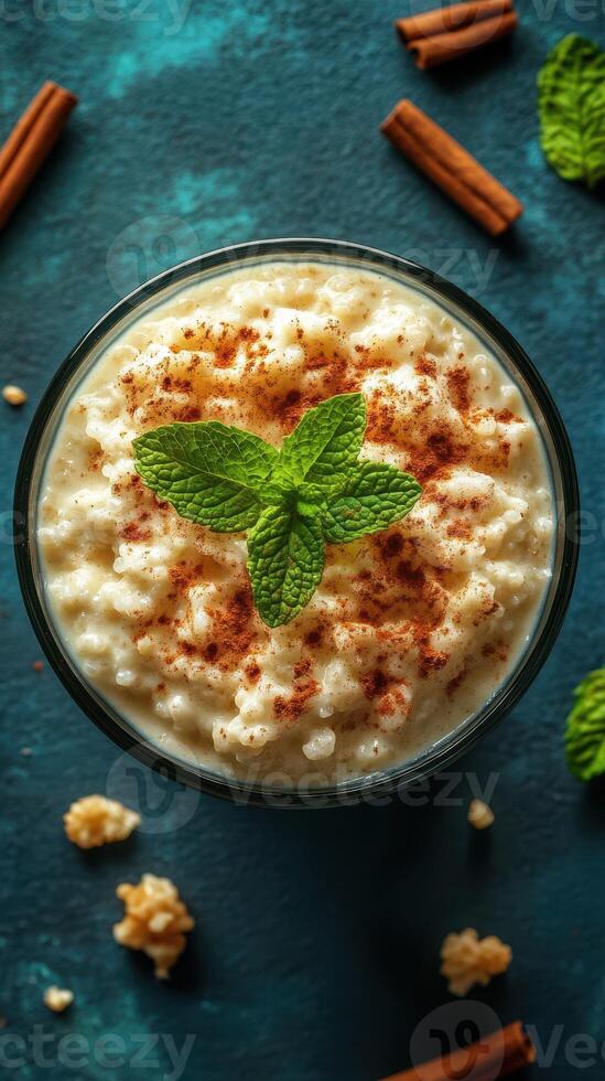 Creamy rice pudding topped with cinnamon and mint leaves on a textured blue background photo