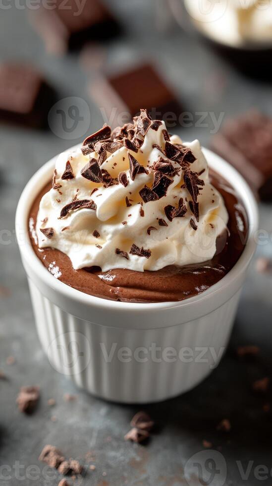 Creamy chocolate mousse topped with whipped cream and chocolate shavings served in a white ramekin on a dark countertop photo