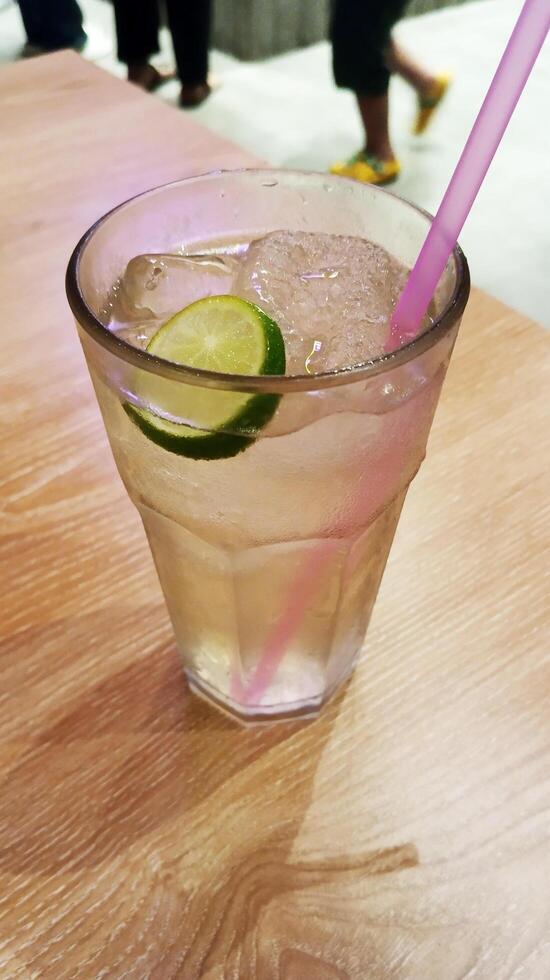 Lemon drink glass with green lemon or lime with pink straw on wooden table of restaurant. photo