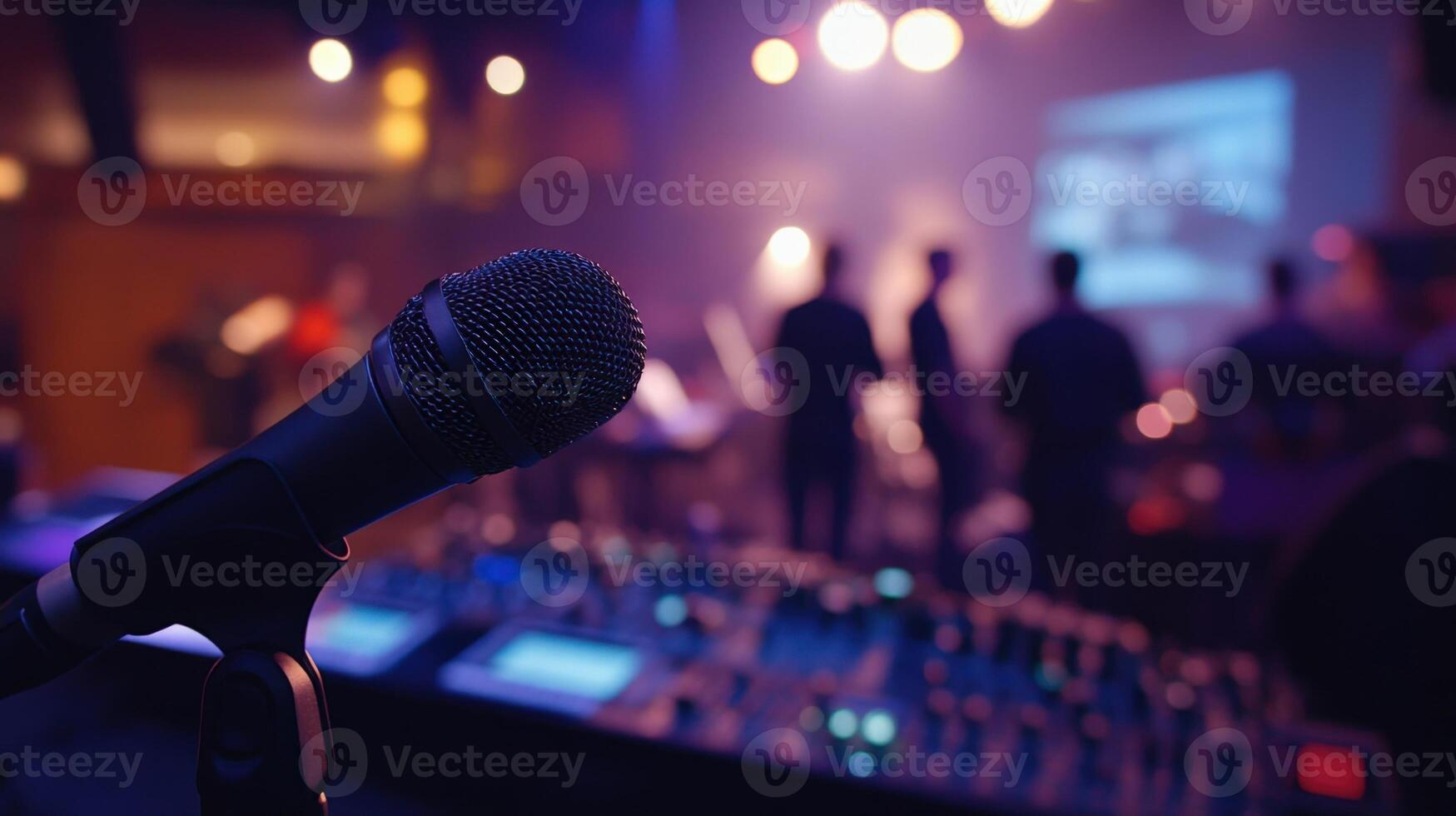 Closeup of a handheld microphone in the foreground with blurred figures of crew members in the background as they communicate and finetune the sound setup before the live event begins photo