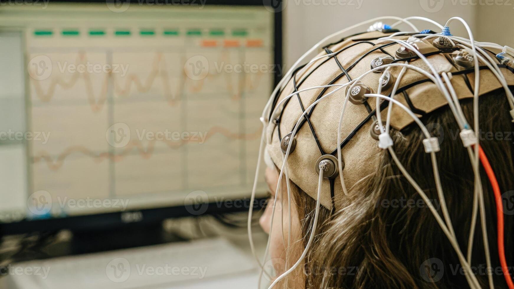 A detailed view of an EEG cap on a human head with electrodes attached to the scalp and data streaming on a nearby monitor visually representing the bridge between neural signals. photo