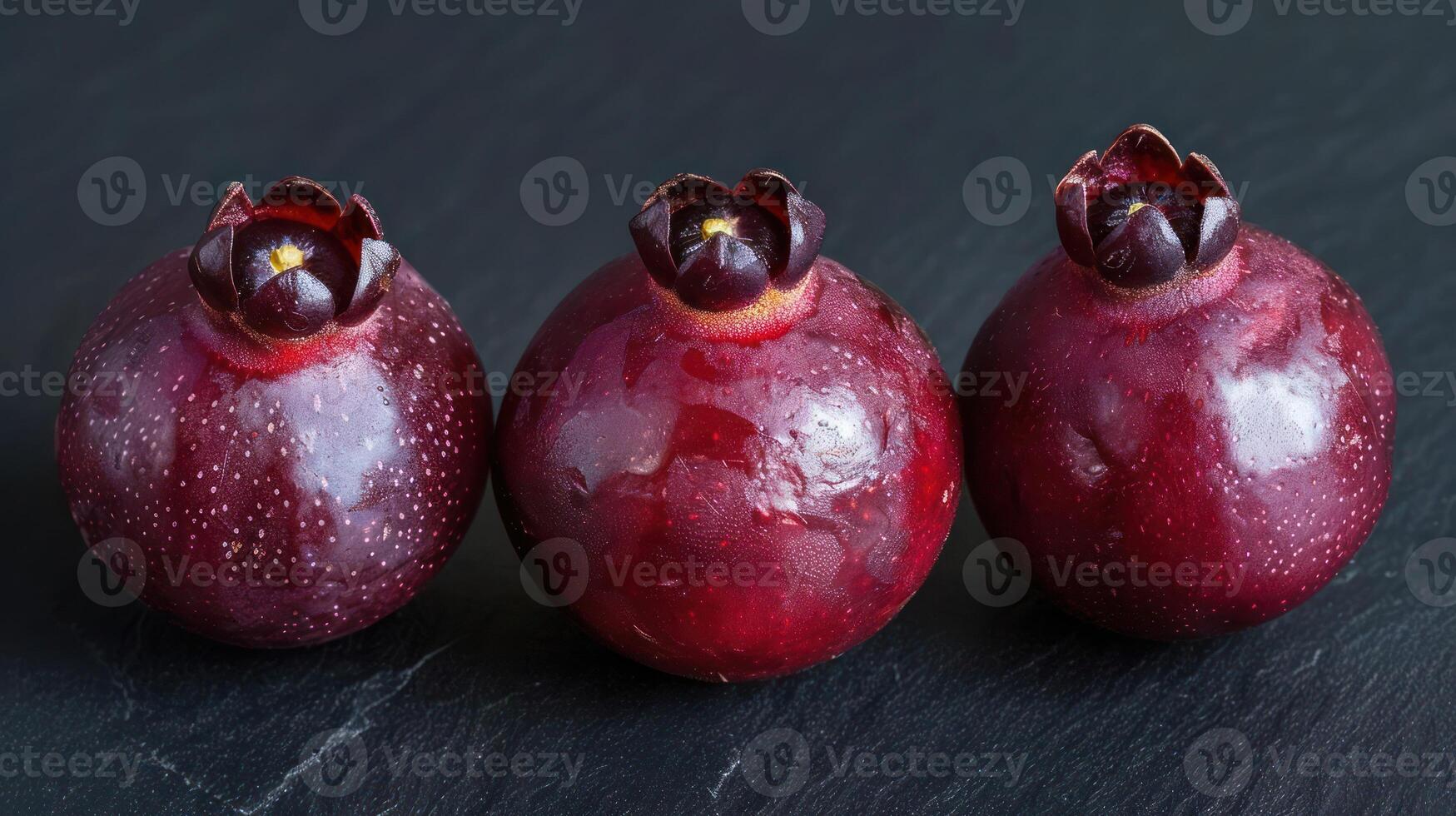 Three glossy, dark red fruits displayed on a slate surface. photo