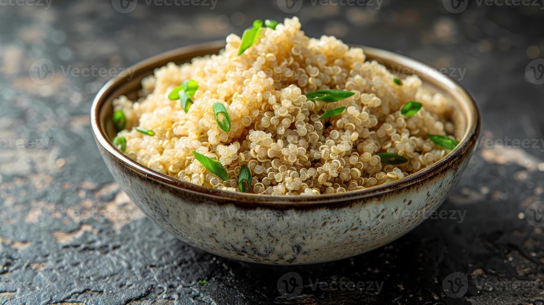 A bowl of cooked quinoa garnished with chopped green onions on a textured surface. photo
