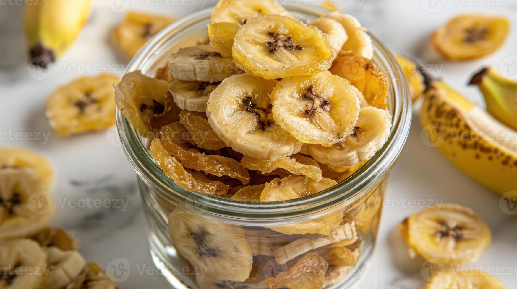 A glass jar filled with dried banana slices, surrounded by fresh bananas on a marble surface. photo