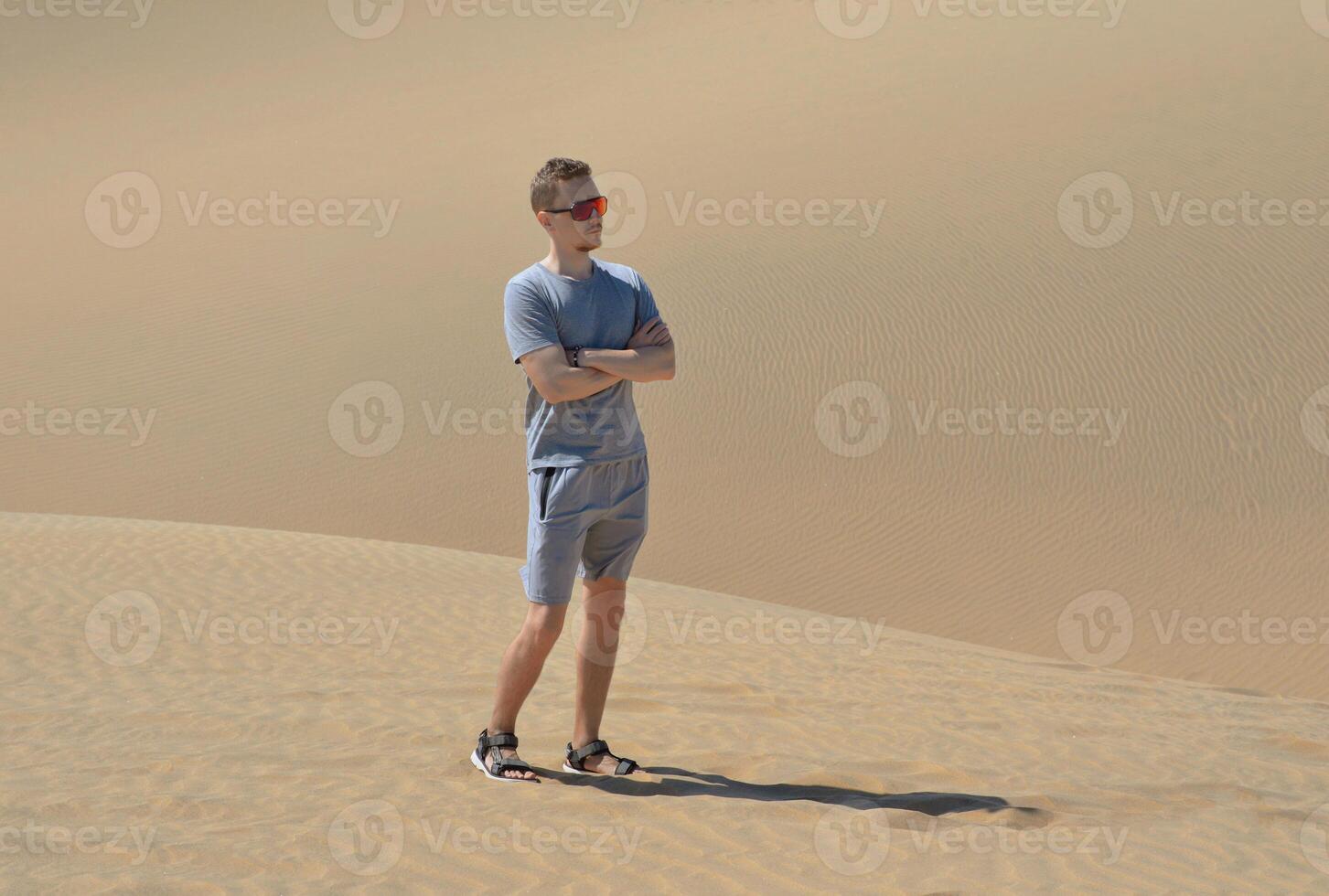 A man in a desert. A young man wearing red sunglasses standing at the sand barchan background. Dune in Maspalomas, Gran Canaria photo