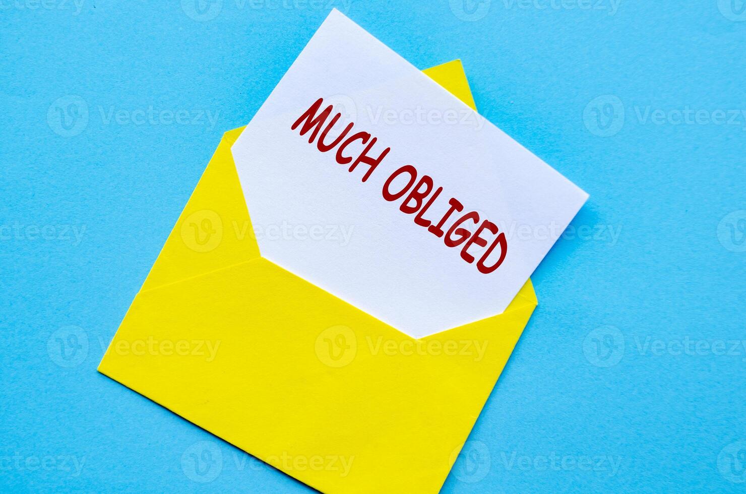 Yellow envelope on a blue cover with a white card partially pulled out with Much Obliged text photo