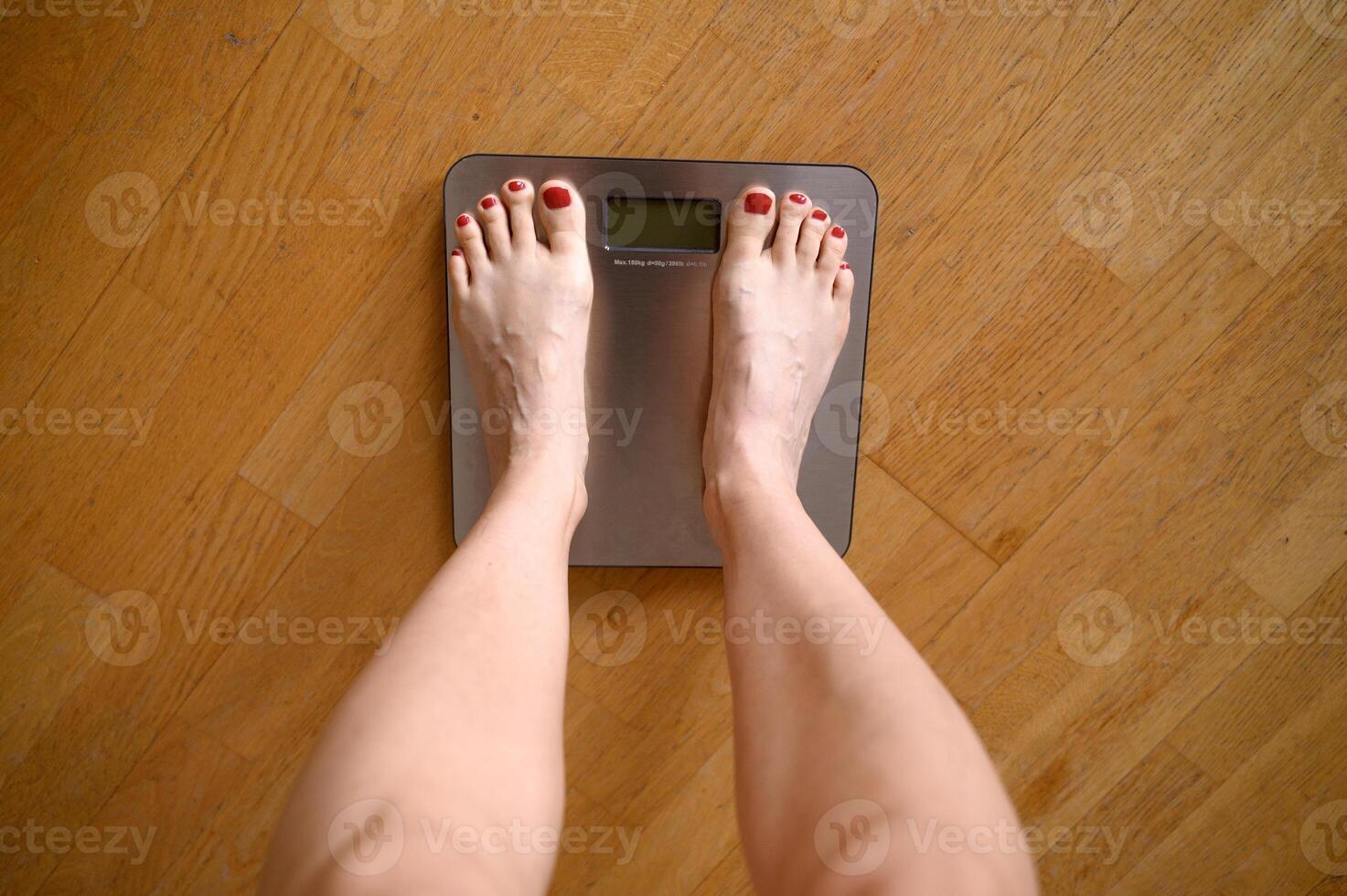 Woman feet with red nail polish on the bathroom scales photo