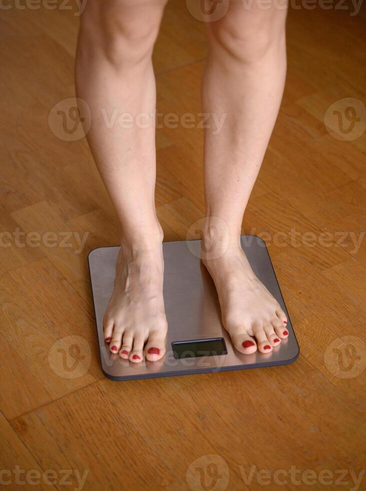 Woman feet with red nail polish on the bathroom scales photo