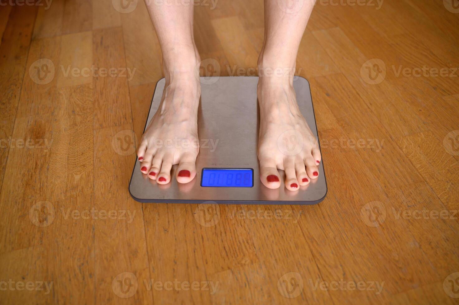 Woman feet with red nail polish on the bathroom scales photo