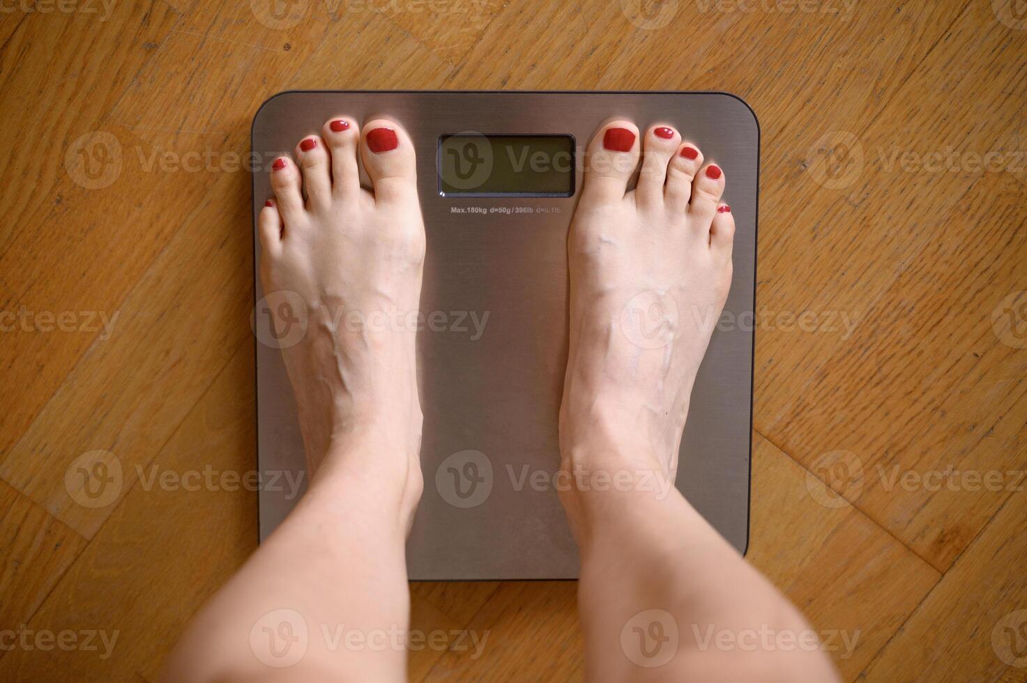Woman feet with red nail polish on the bathroom scales photo