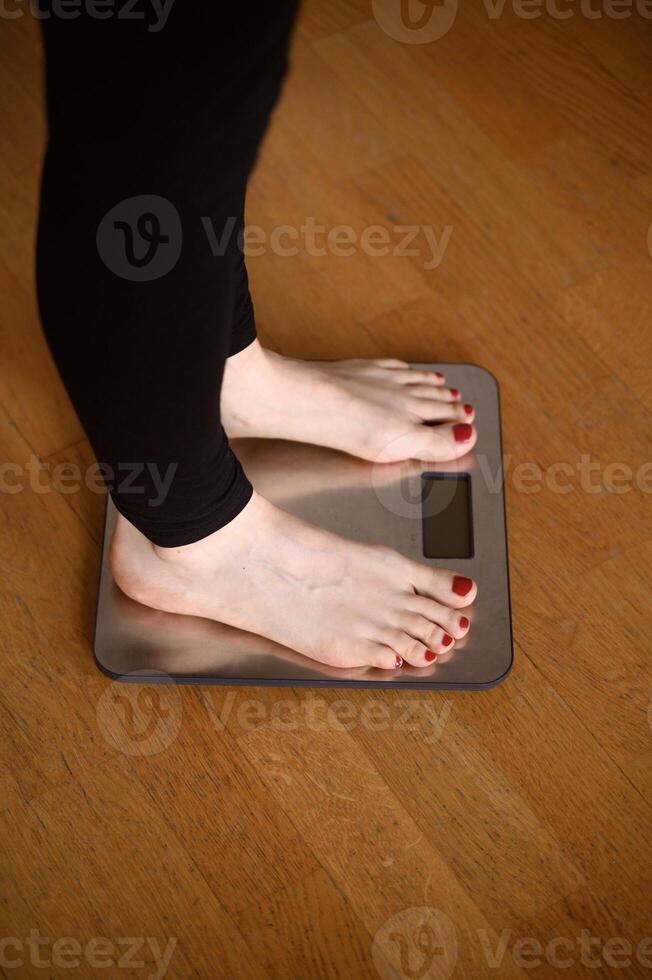 Woman feet with red nail polish on the bathroom scales photo