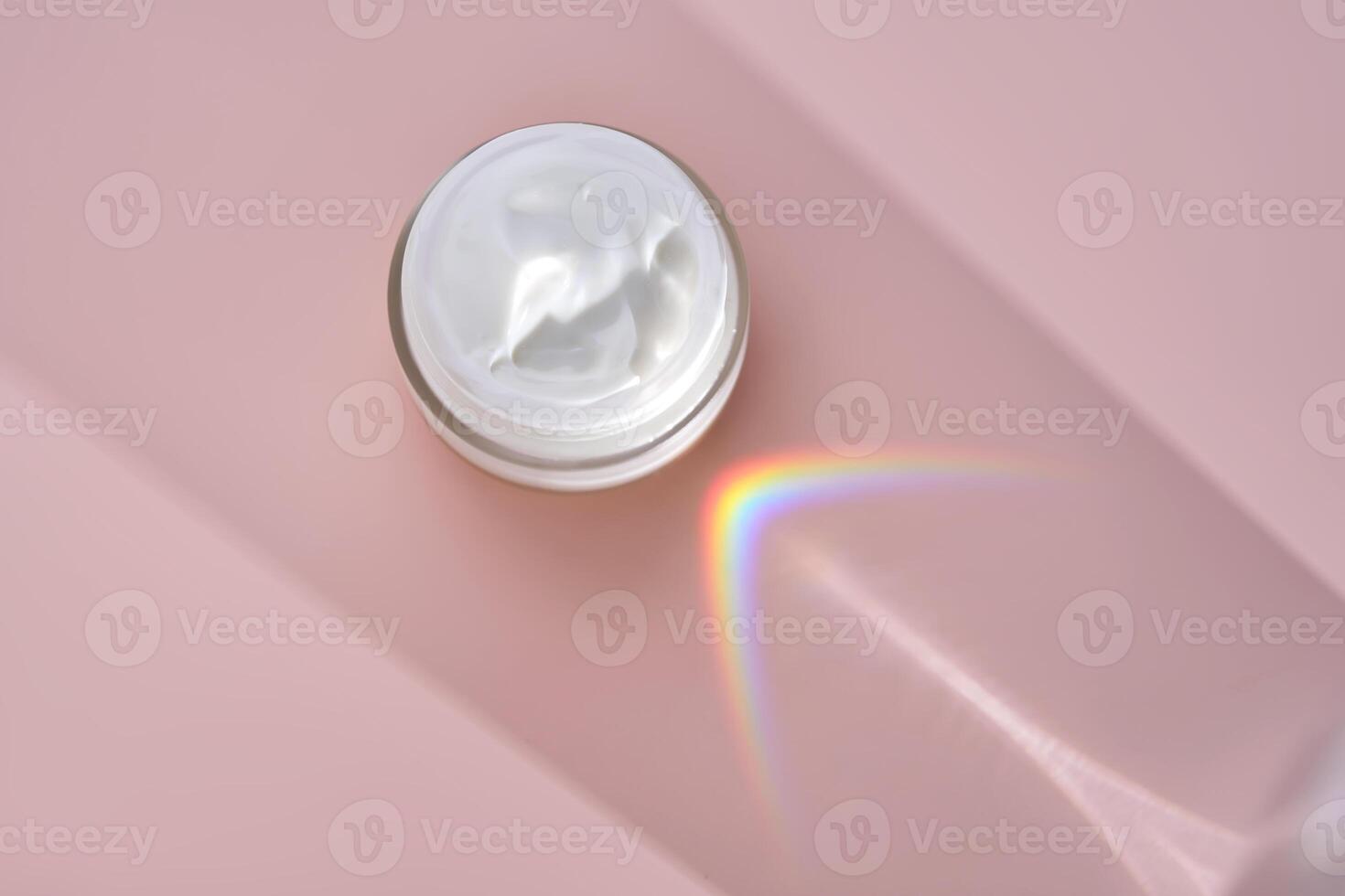 An open jar of cream with its texture on a pink background. photo