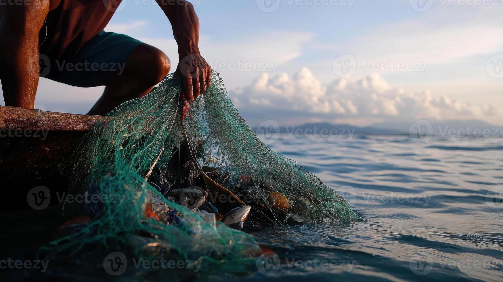fisherman pulling up his net filled with fish at sunset photo