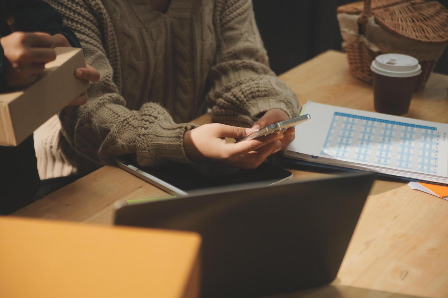 A person using a laptop and a phone while sitting at a table photo