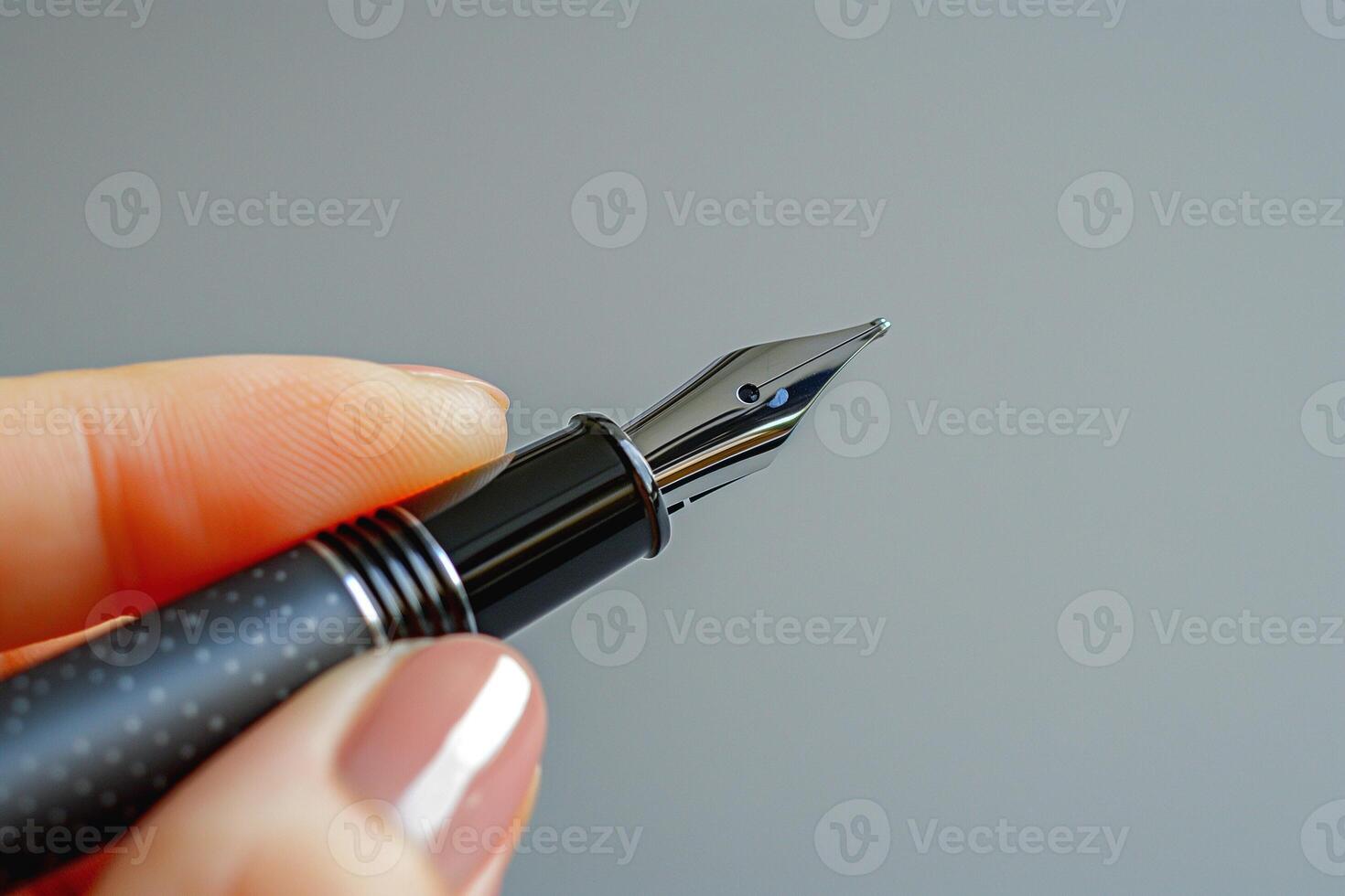 Close-up of a woman's hand holding a sleek black fountain pen against a gray background. photo