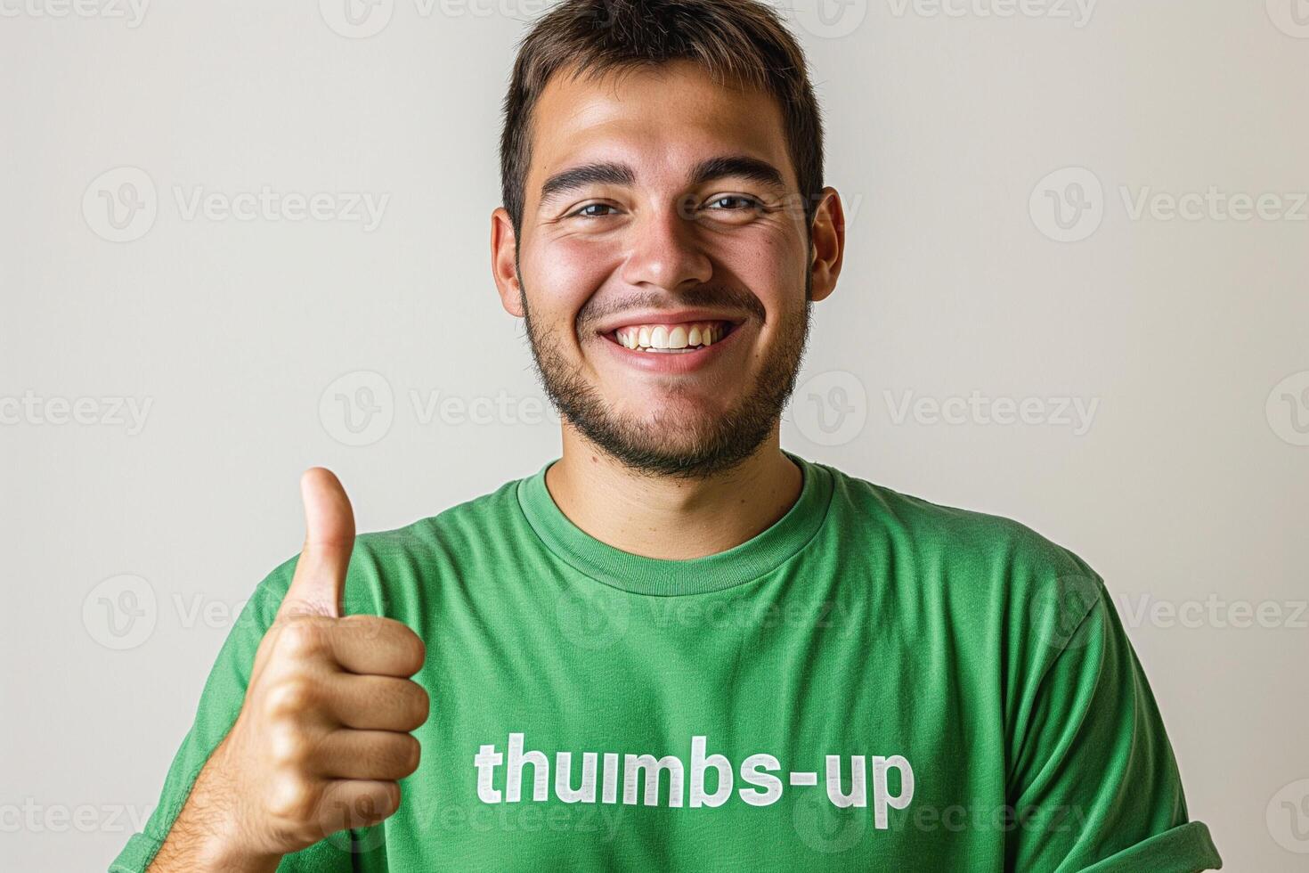 A smiling young man with a light beard gives a thumbs up while wearing a green shirt, exuding positivity and enthusiasm. photo