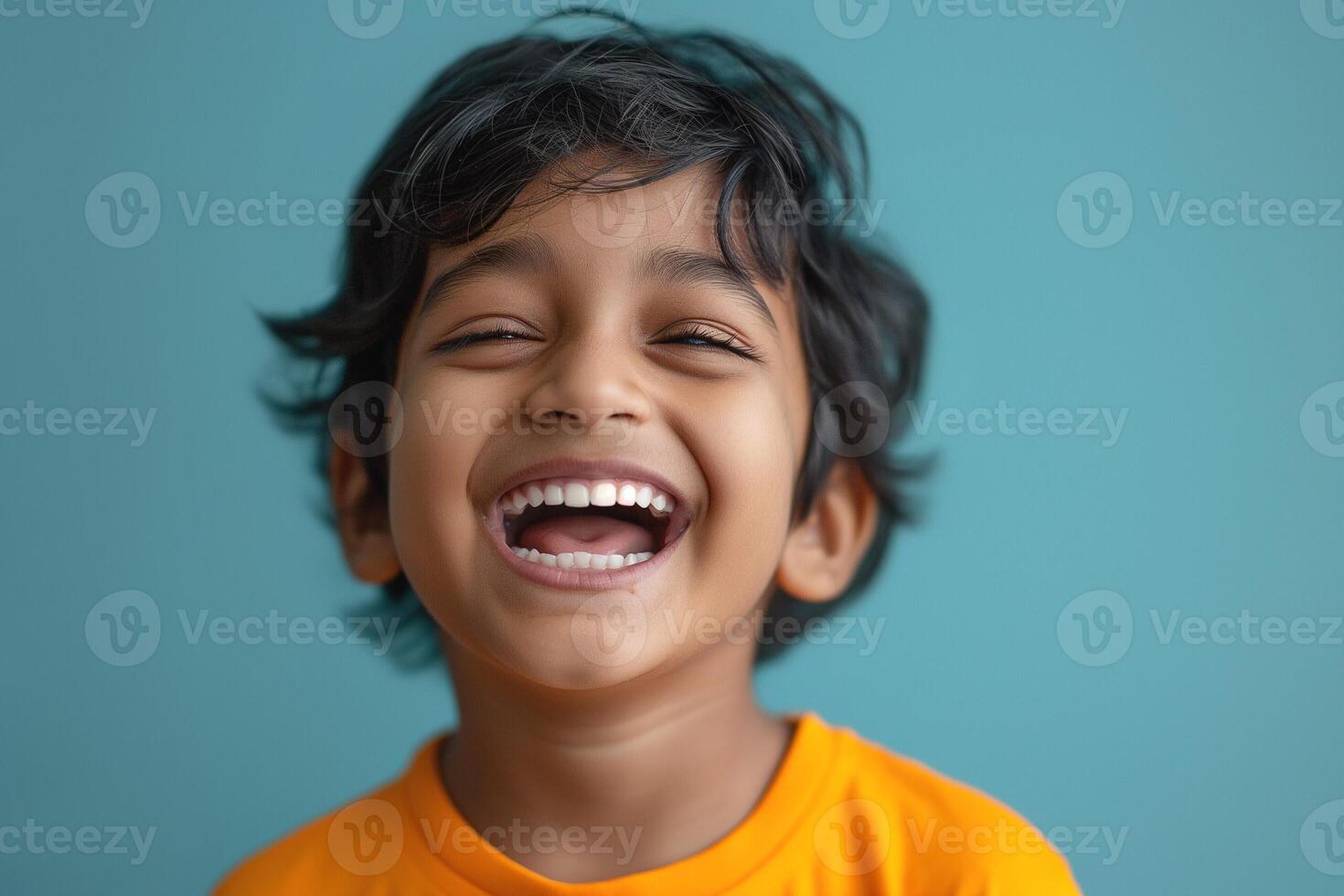 Cheerful young boy with curly hair laughing joyfully against a turquoise background. photo