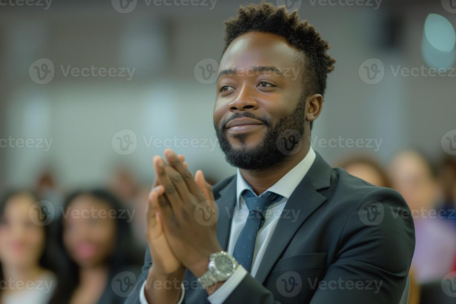 A focused Black man in a suit actively applauding during a formal event, showcasing engagement and positive energy. photo