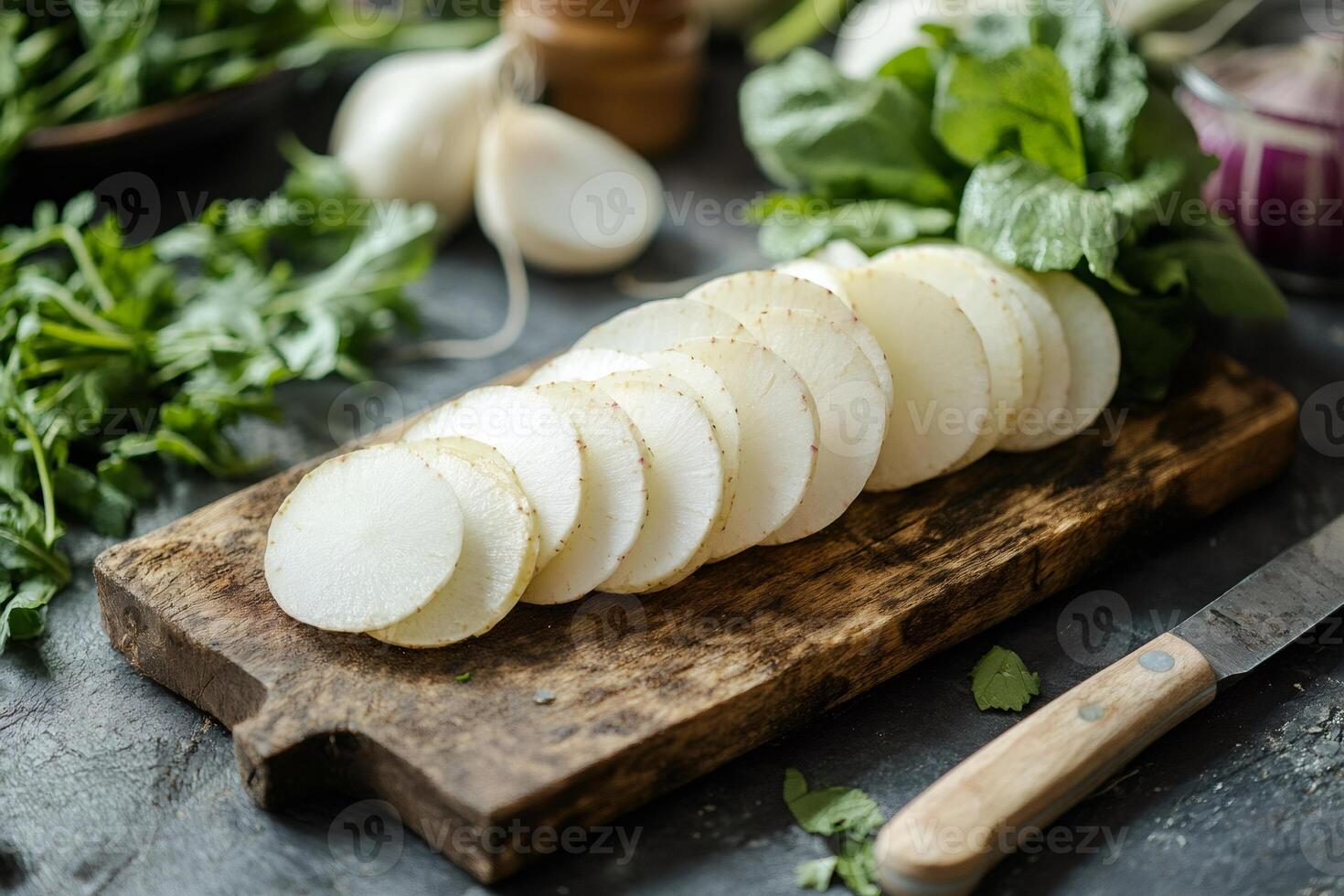 Sliced daikon radish on cutting board with fresh herbs and knife photo
