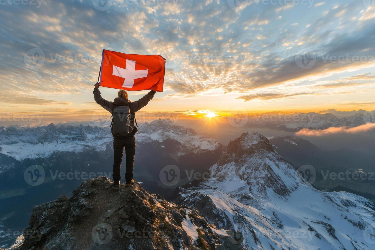 Hiker is holding Swiss flag on top of a mountain at sunrise photo