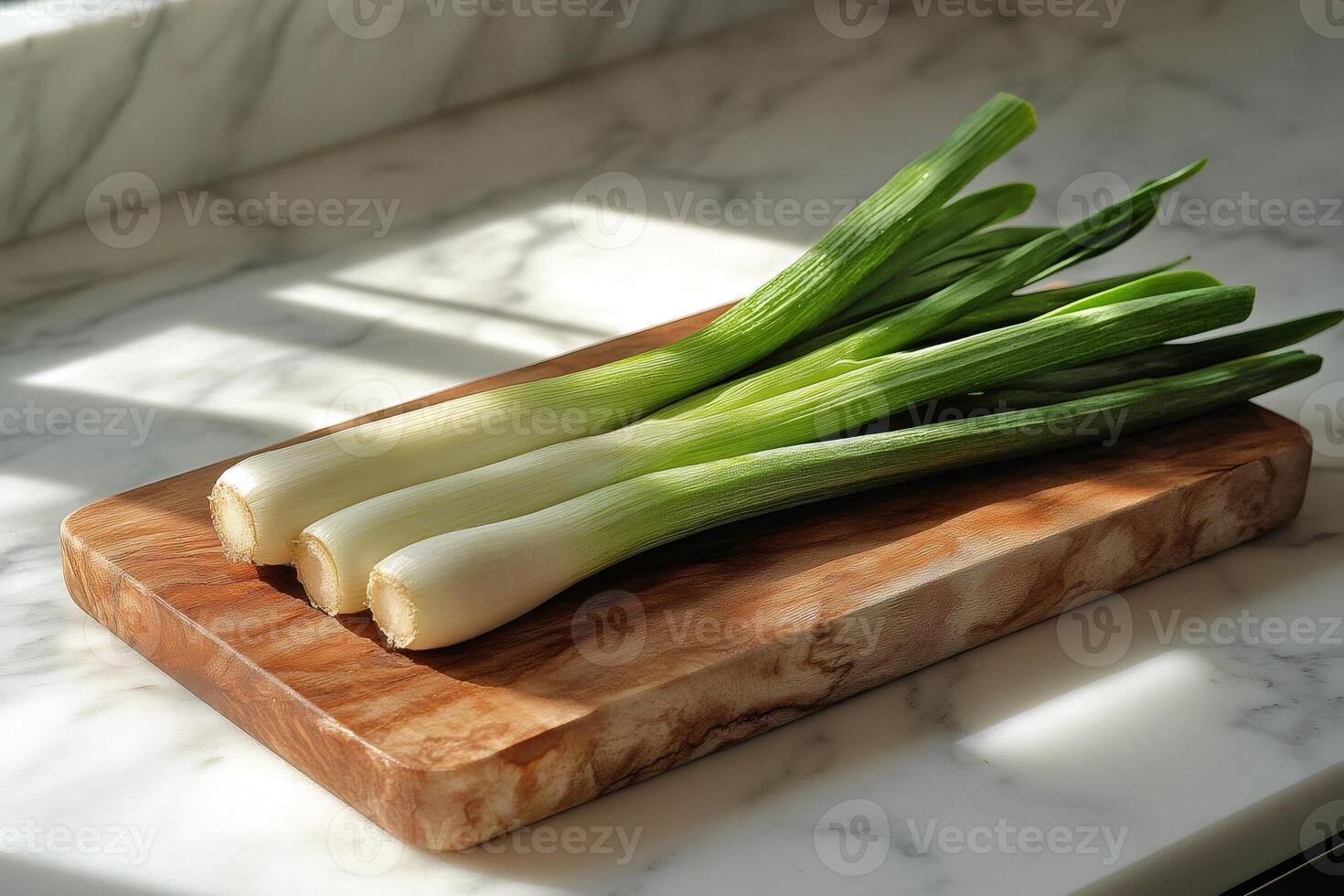 Fresh spring onions resting on a wooden cutting board in a sunlit kitchen photo