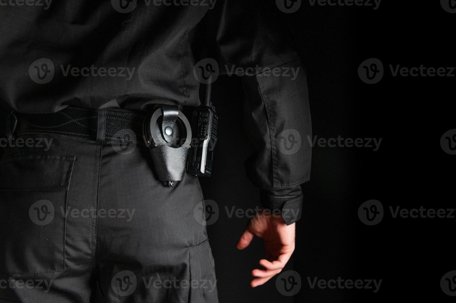 security guard controlling the premises. bodyguard in black uniform on black background, with handcuffs on his belt photo