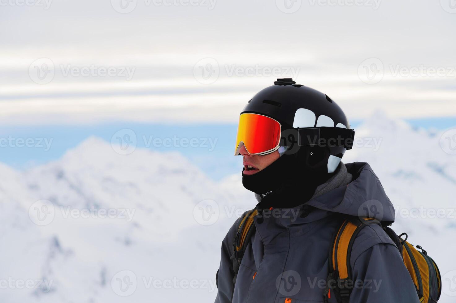 Photo of smiling man with alpine skis or snowboard, mountains and sunset in the background. Enjoying vacation at resort, relaxed lifestyle