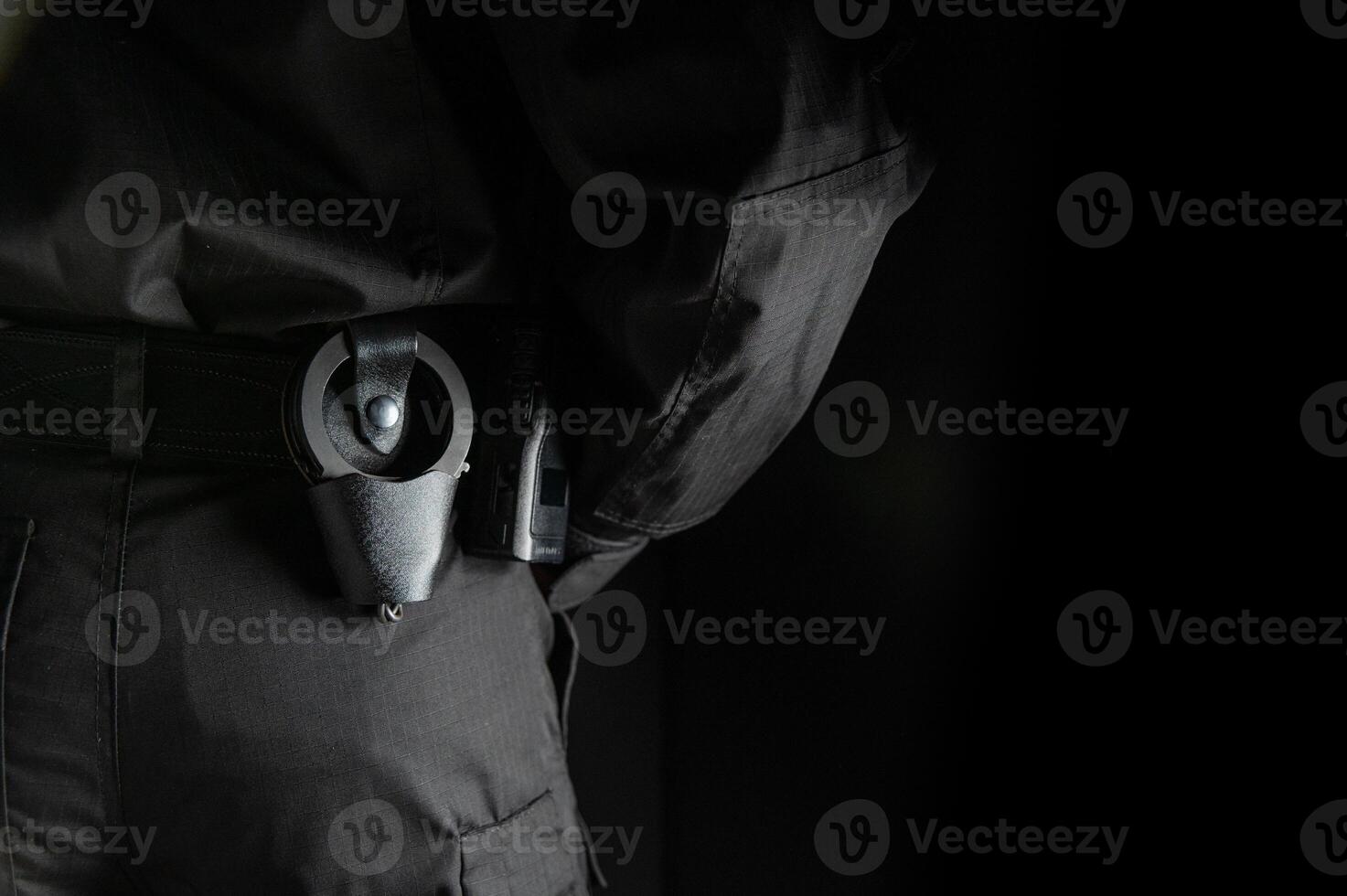 security guard controlling the premises. bodyguard in black uniform on black background, with handcuffs on his belt photo