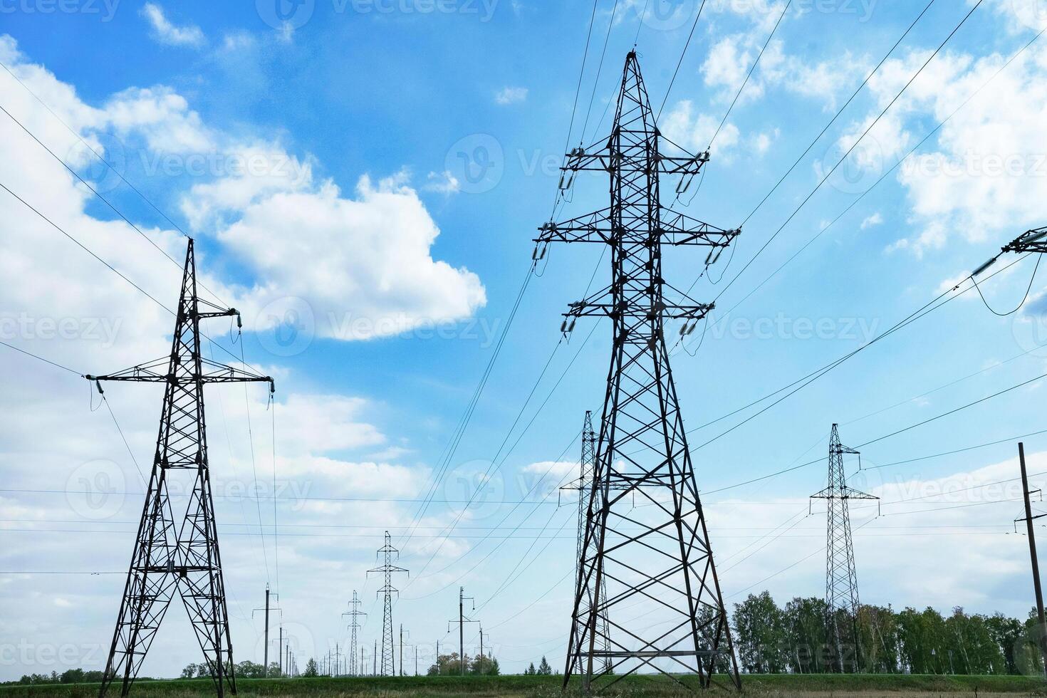 High voltage power lines leading through a green field. On a sunny day Transmission of electricity by means of supports through agricultural areas. photo