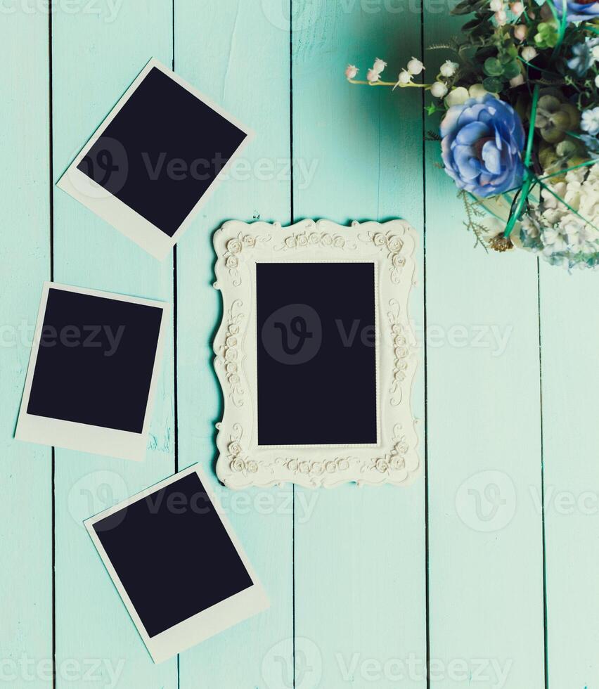 Decorative empty photo frame and blank polaroids on a teal wooden surface with a bouquet of flowers