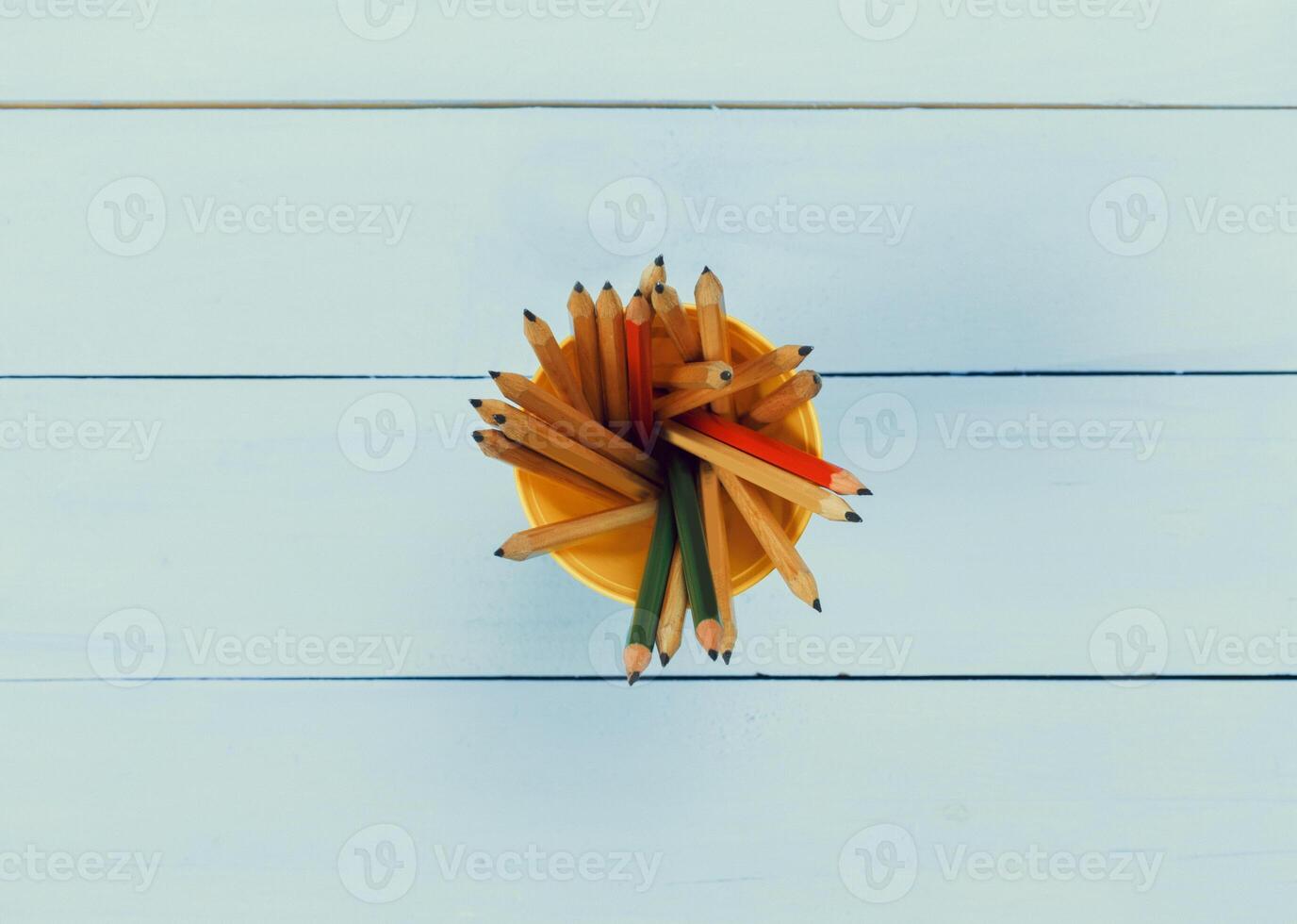 Colorful pencils arranged neatly in a yellow holder on a light wooden surface during daylight photo