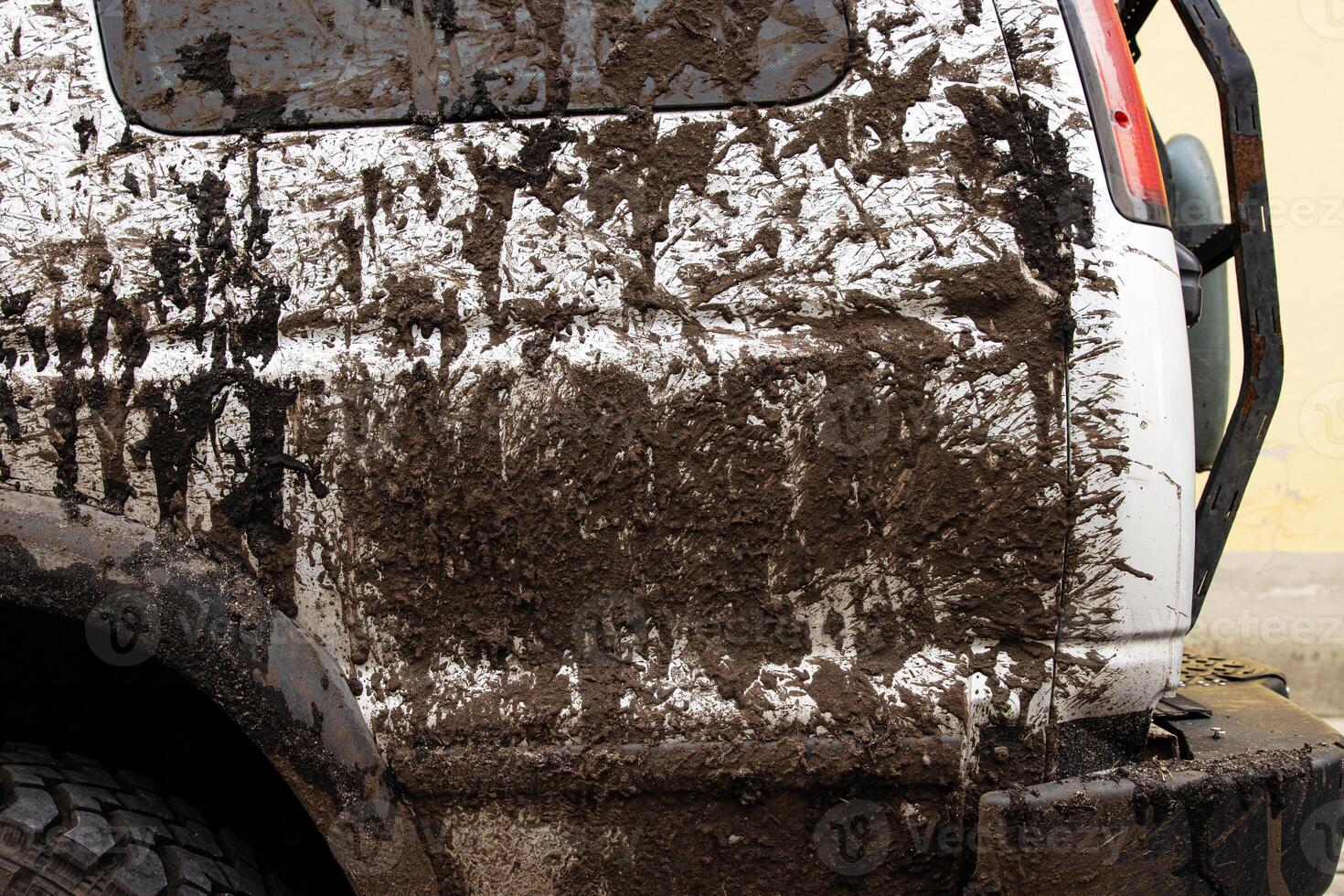 Dirty 4x4 vehicle with mud splatters on the body, wheels tires, rear bumber. Closeup of a muddy offroad suv car covered in dirt. Importance of car wash, maintenance, and safe driving concept photo