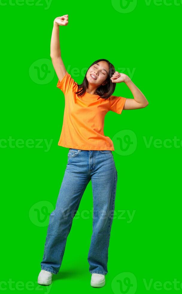 Young woman in orange shirt happily dancing against bright green background during a joyful moment photo
