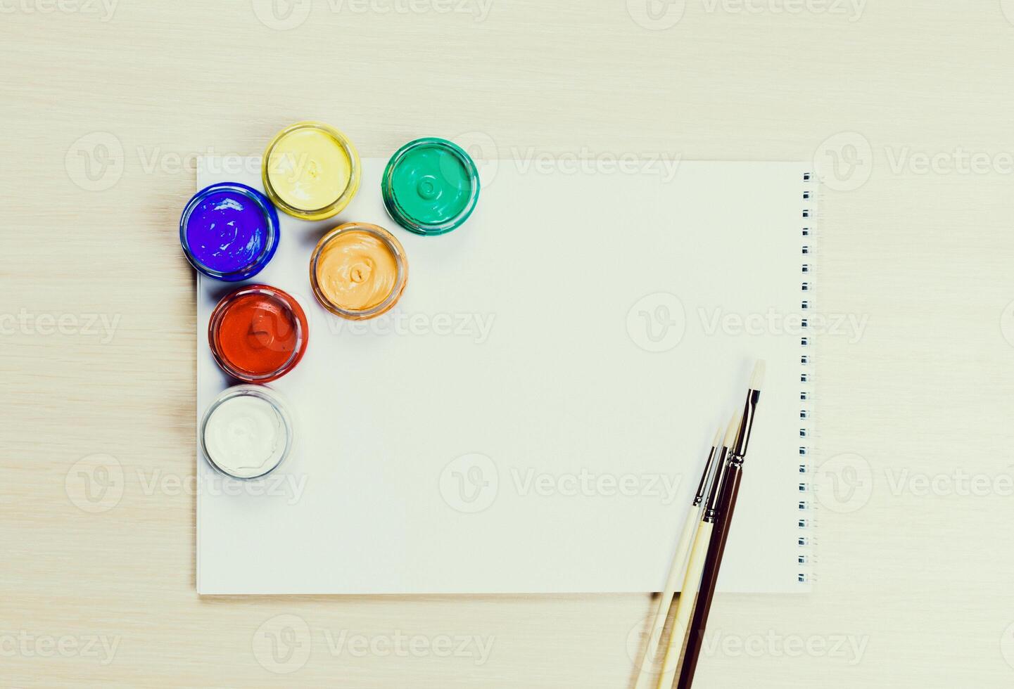Colorful paints and brushes arranged on a blank sketchpad ready for creative expression photo