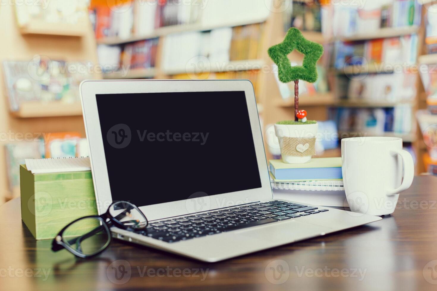 Cozy workspace with laptop, coffee, and decorative plant in a vibrant bookshop setting photo