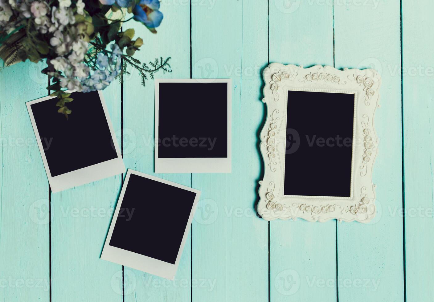 Blank pictures and a decorative frame arranged on a wooden table with a floral arrangement nearby photo