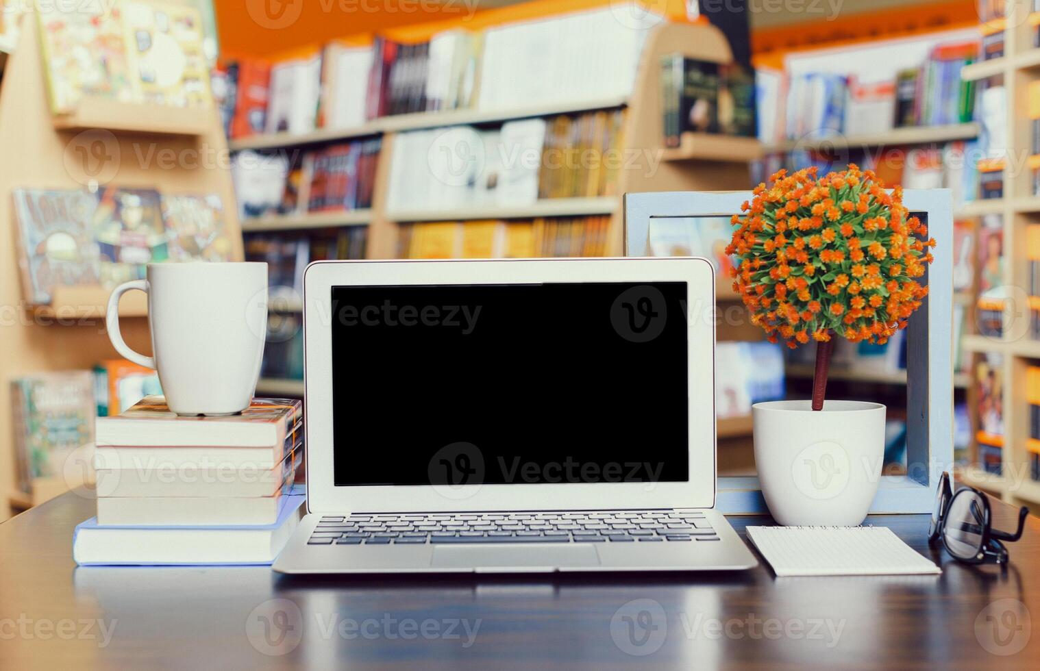 Workspace setup in a cozy bookstore featuring a laptop, books, coffee, and plants photo